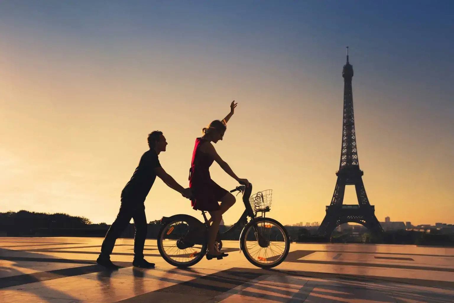 Couple sur un vélo devant la tour Eiffel au coucher du soleil