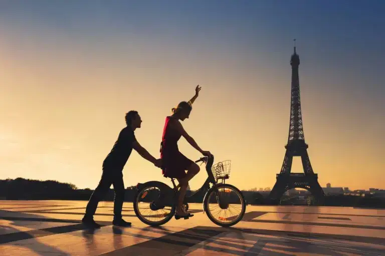 Couple sur un vélo devant la tour Eiffel au coucher du soleil